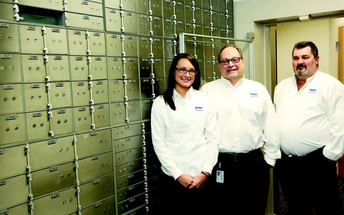 Image of three employees standing beside a wall of security boxes.