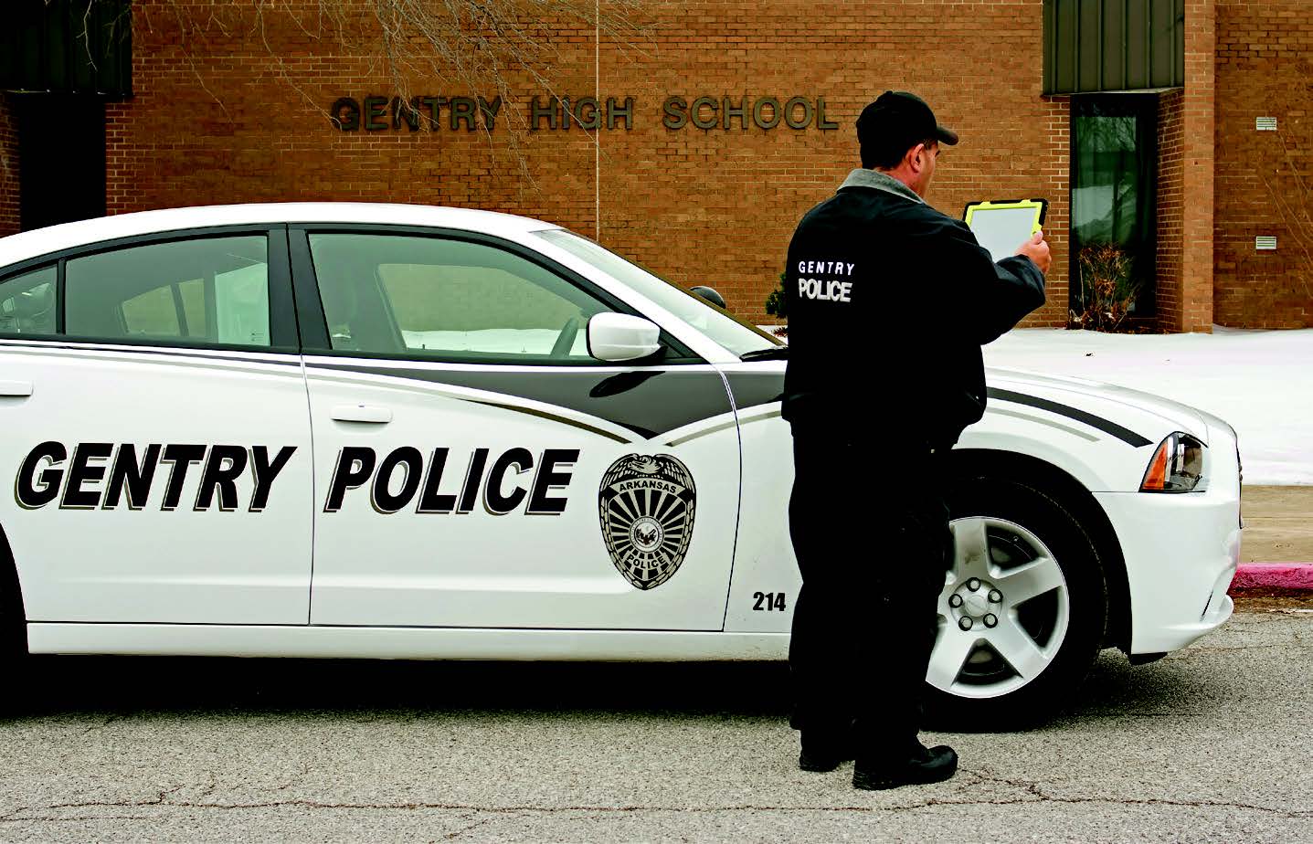 Image of a Gentry police officer on their iPad outside of a Gentry High School. 