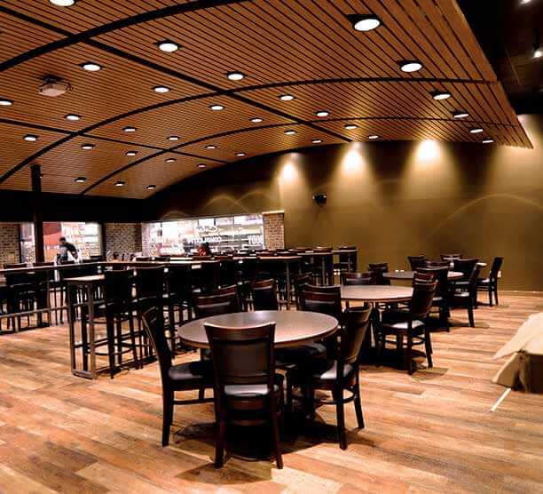 Image of a large wine testing area with tables and bar type seating, curved wood ceiling and an industrial kitchen in the background. 